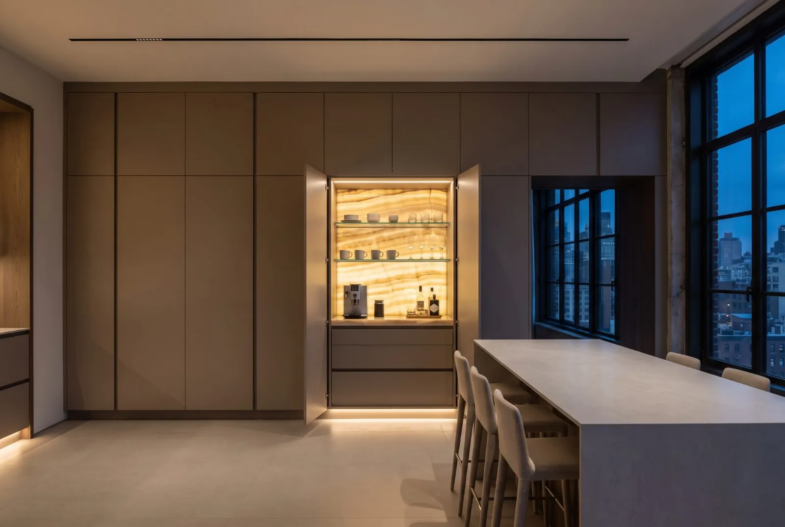 A taupe lacquer kitchen wall open to a coffee niche of backlit onyx